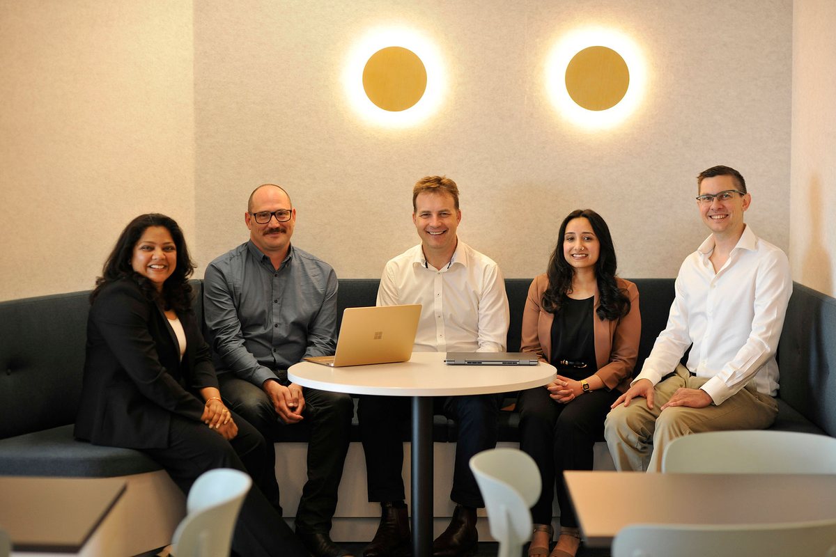 Five members of the Hypergen team seated around a table with laptops, smiling