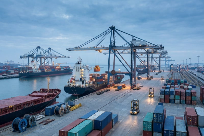 Cranes loading containers onto cargo ships at a busy freight terminal at dusk